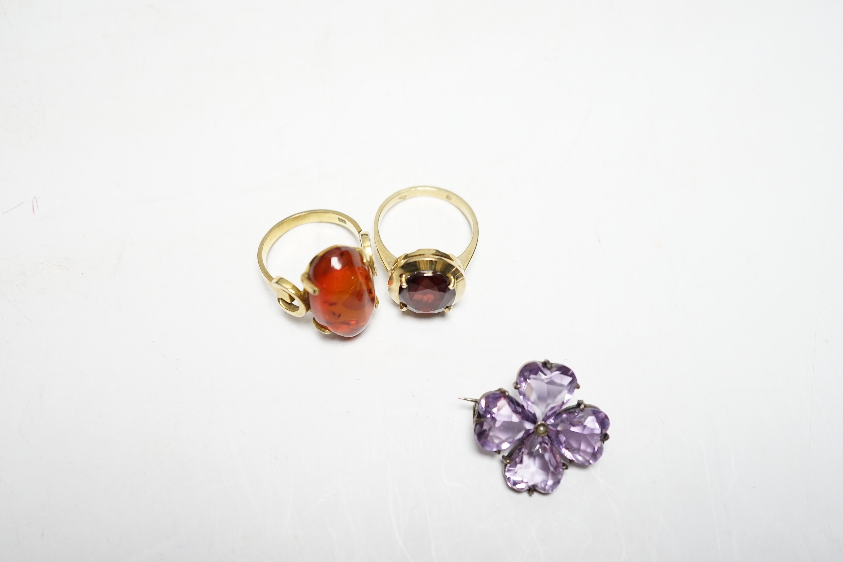 A 333 yellow metal and amber set ring, a 585 and gem set ring and an amethyst and seed pearl set white metal brooch.